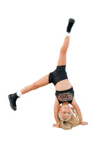 A child performing a handstand in STUDIO ESSENTIALS - SHORTS and a crop top, showcasing activewear flexibility.
