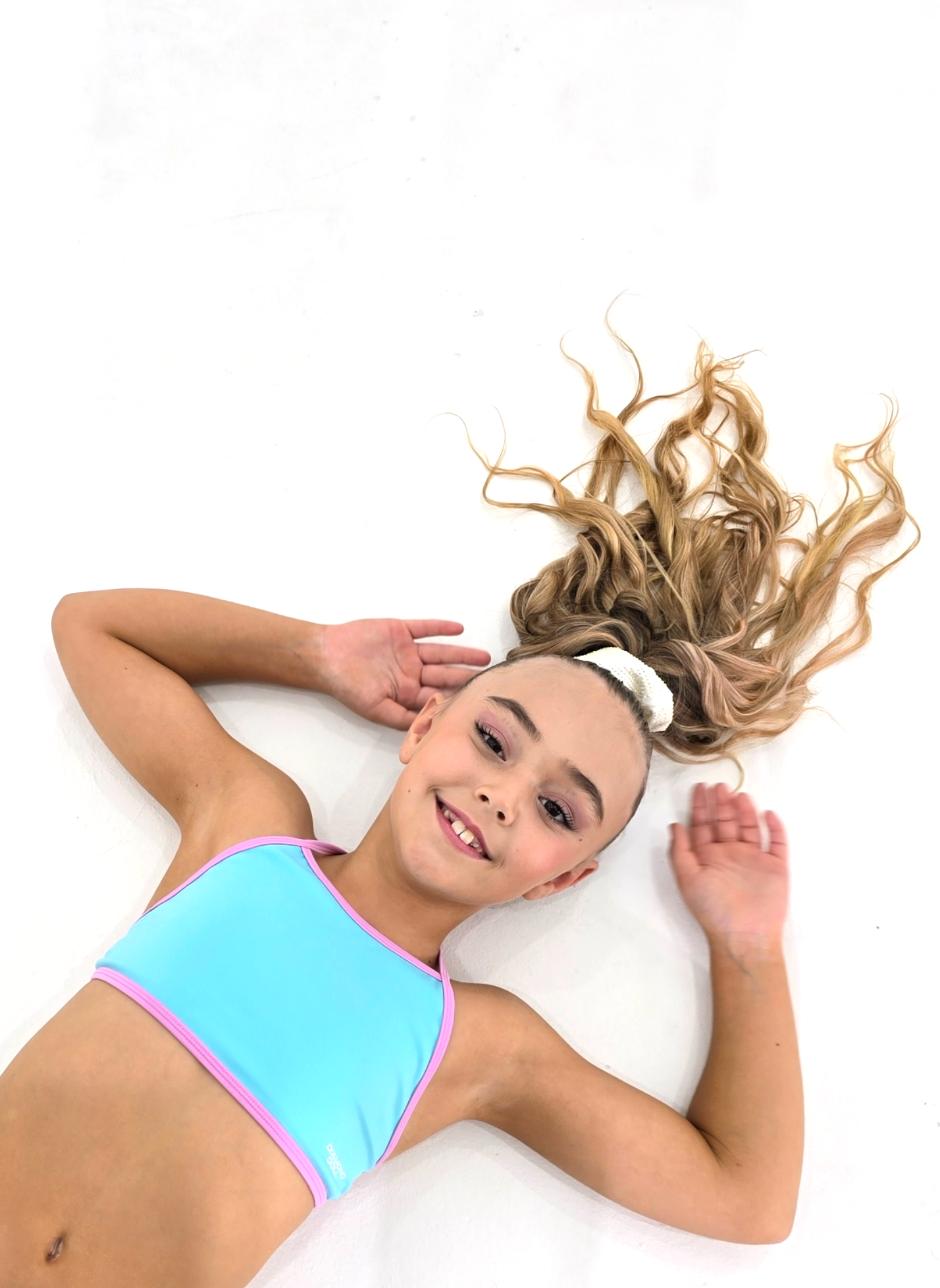 Blue Crush - Crop on a young athlete with long hair laying on a white surface, showcasing the pastel activewear.