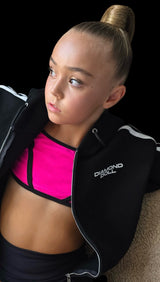 Woman wearing a black jacket with 'Diamond Doll' branding, pink sports bra, and black leggings on a black background.