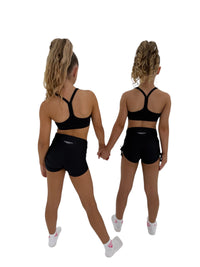 Two young dancers wearing STUDIO CROP tops and black shorts, holding hands, showcasing style and movement.