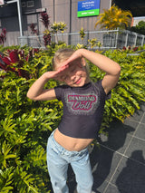 Girl posing in a Diamond Doll Baby Tee surrounded by vibrant greenery outdoors.