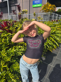 Girl posing in a Diamond Doll Baby Tee surrounded by vibrant greenery outdoors.