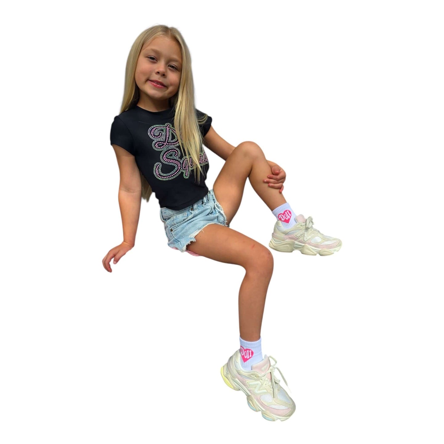 Girl in a black shirt and denim shorts wearing Doll Socks with pink hearts and stylish sneakers.