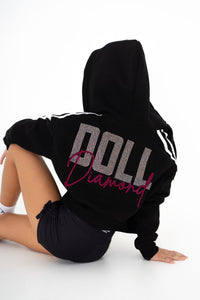 Person wearing a black hoodie with 'DOLL' text, sitting on a white background