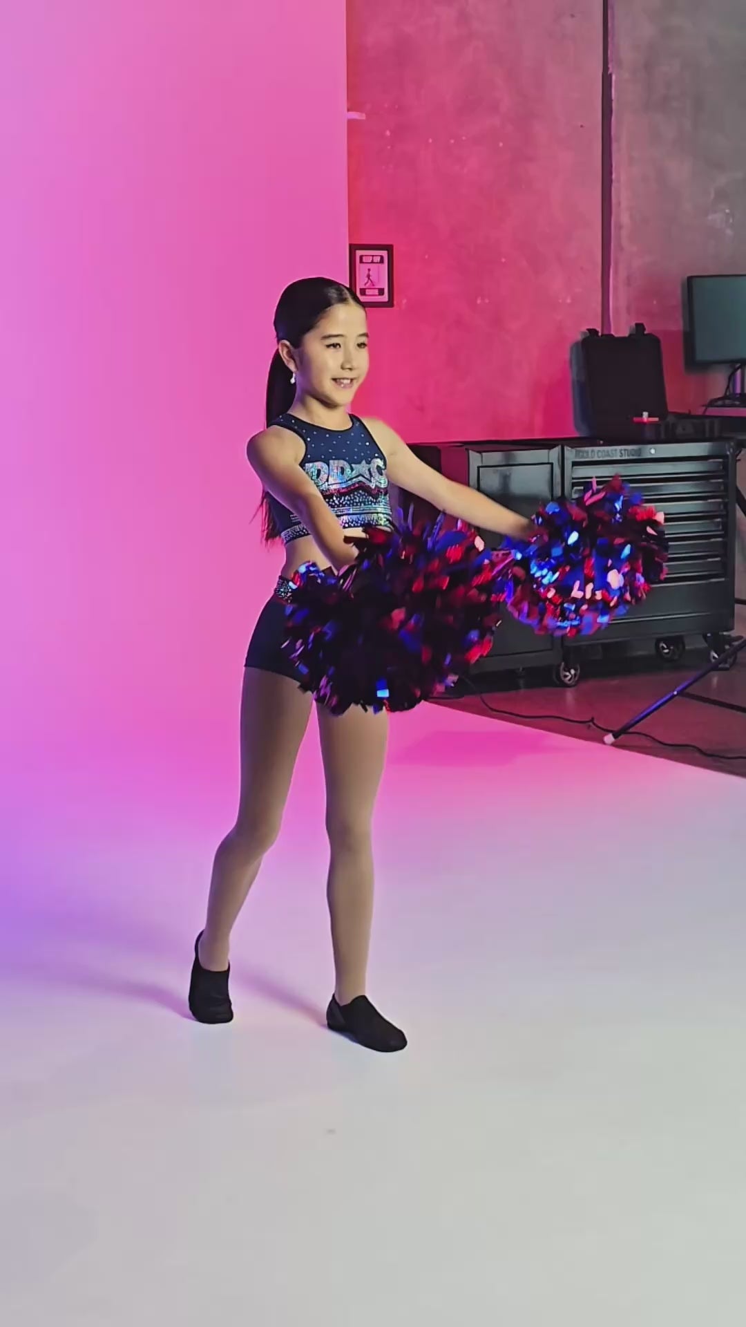DDC Navy Rhinestone - Crop worn by a young dancer posing with pom poms under vibrant lights.